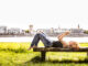 Germany, Cologne, redheaded young woman lying on bench taking selfie with cell phone